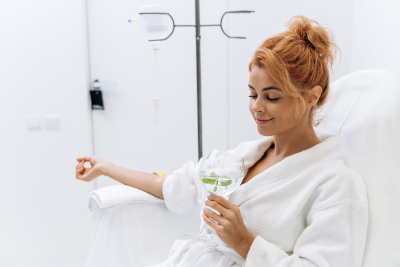 charming woman in white bathrobe sitting in armchair and receiving IV infusion